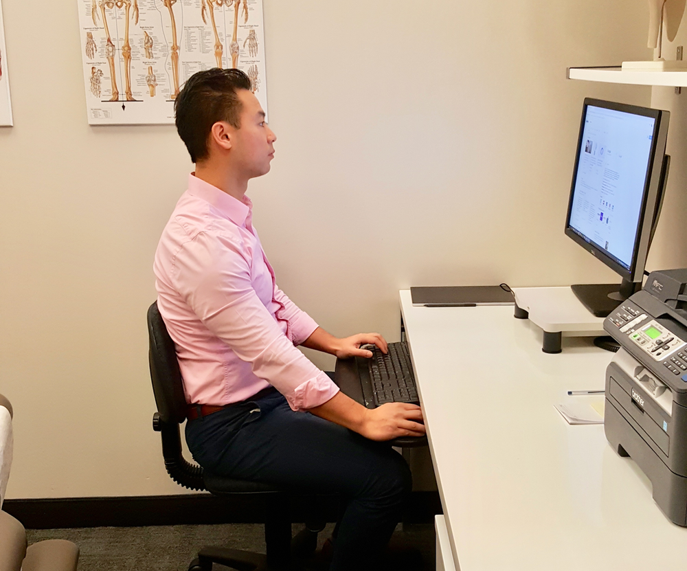 Rebuild physiotherapy Eric Lau demonstrating proper posture at work desk