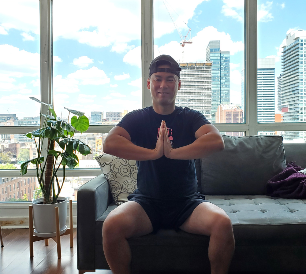 Man sitting on a couch performing the prayer stretch to stretch the front of his forearms.